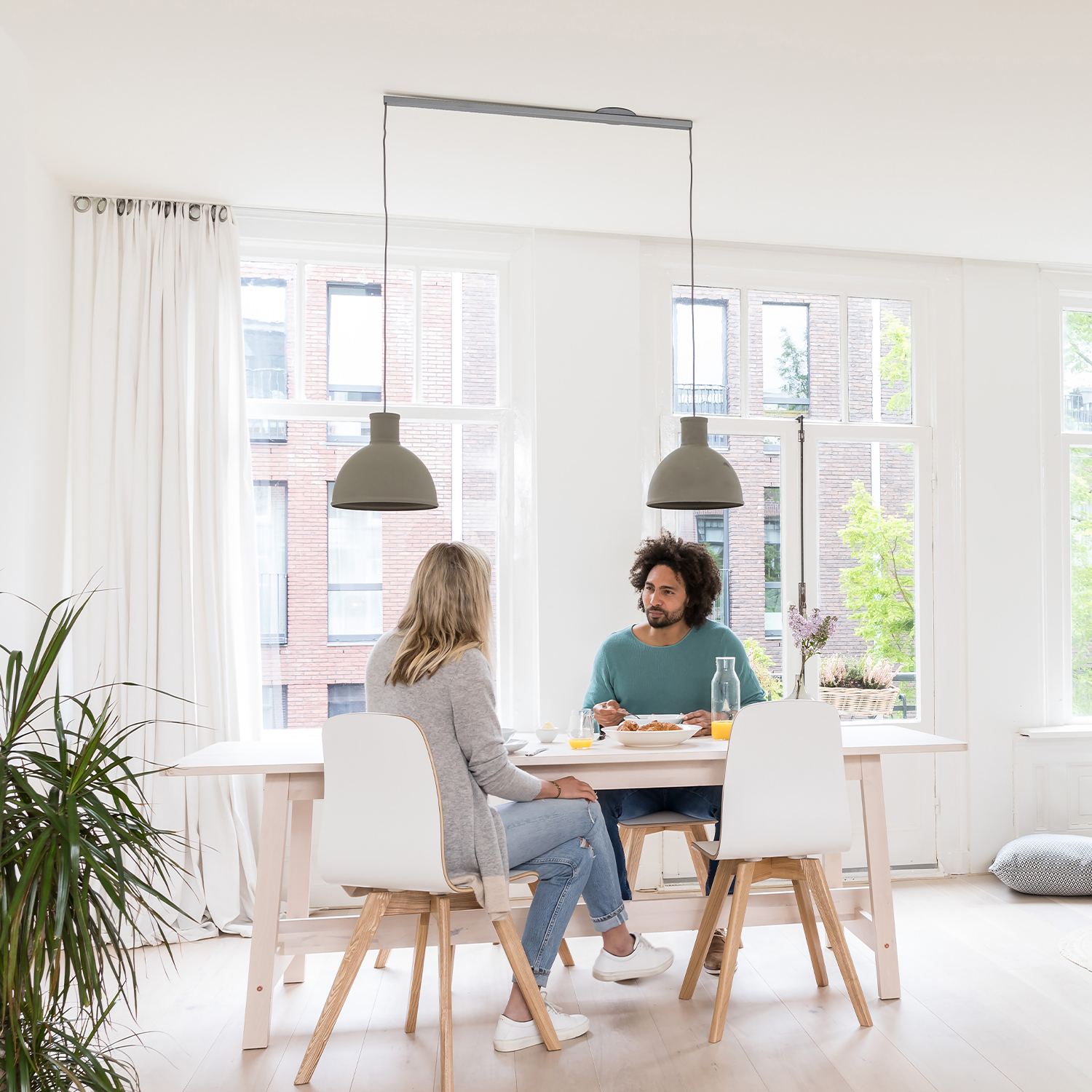 Lightswing RVS gémeos num interior branco com duas pessoas à mesa de jantar.